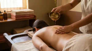 ayurvedic massage dubai session: therapist pouring warm herbal oil from a brass bowl during an abhyanga full body massage in a wooden treatment room