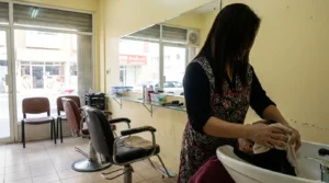 salon in deira: stylist rinsing a clients hair at a basin in a modest ladies salon with worn chairs and a street view through the window