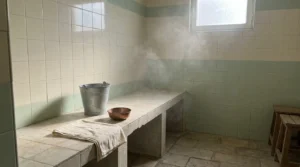 hammam dubai cheap: modest neighbourhood hammam room in an older Dubai district with a tiled washing bench, metal bucket and copper bowl in warm steam